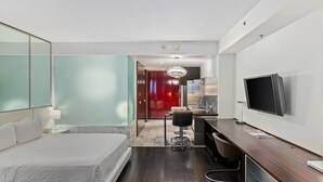 Een moderne hotelkamer met een groot bed, een bureau met een flatscreen-televisie, een stoel en een rode deur op de achtergrond.