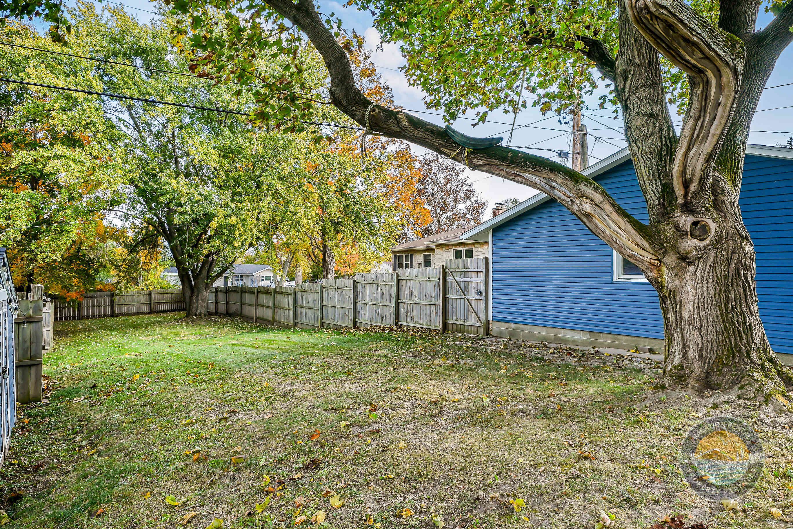 A backyard with a tree, a wooden fence, and a blue house.