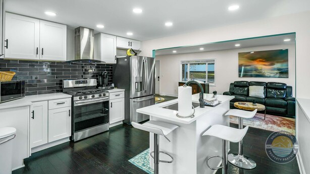 Una cocina moderna con armarios blancos, electrodomésticos de acero inoxidable y una barra con taburetes.