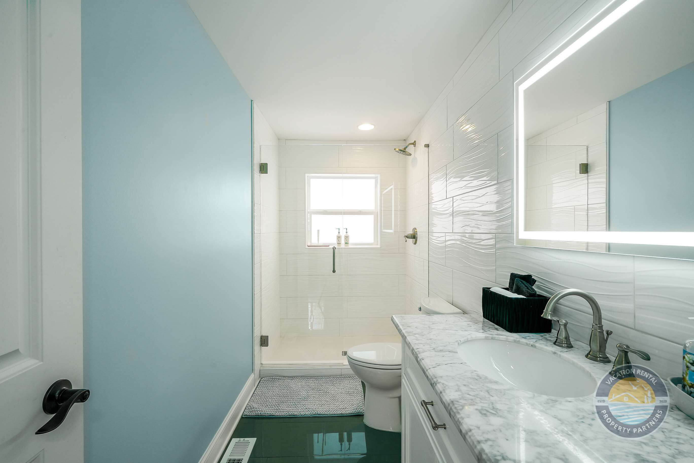 A bathroom with a shower, toilet, sink, and a window.