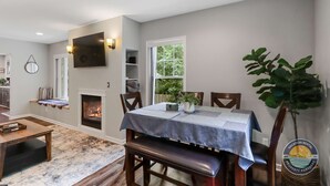 Un área de comedor con una mesa lista para cuatro, una chimenea y vistas de vegetación al exterior.