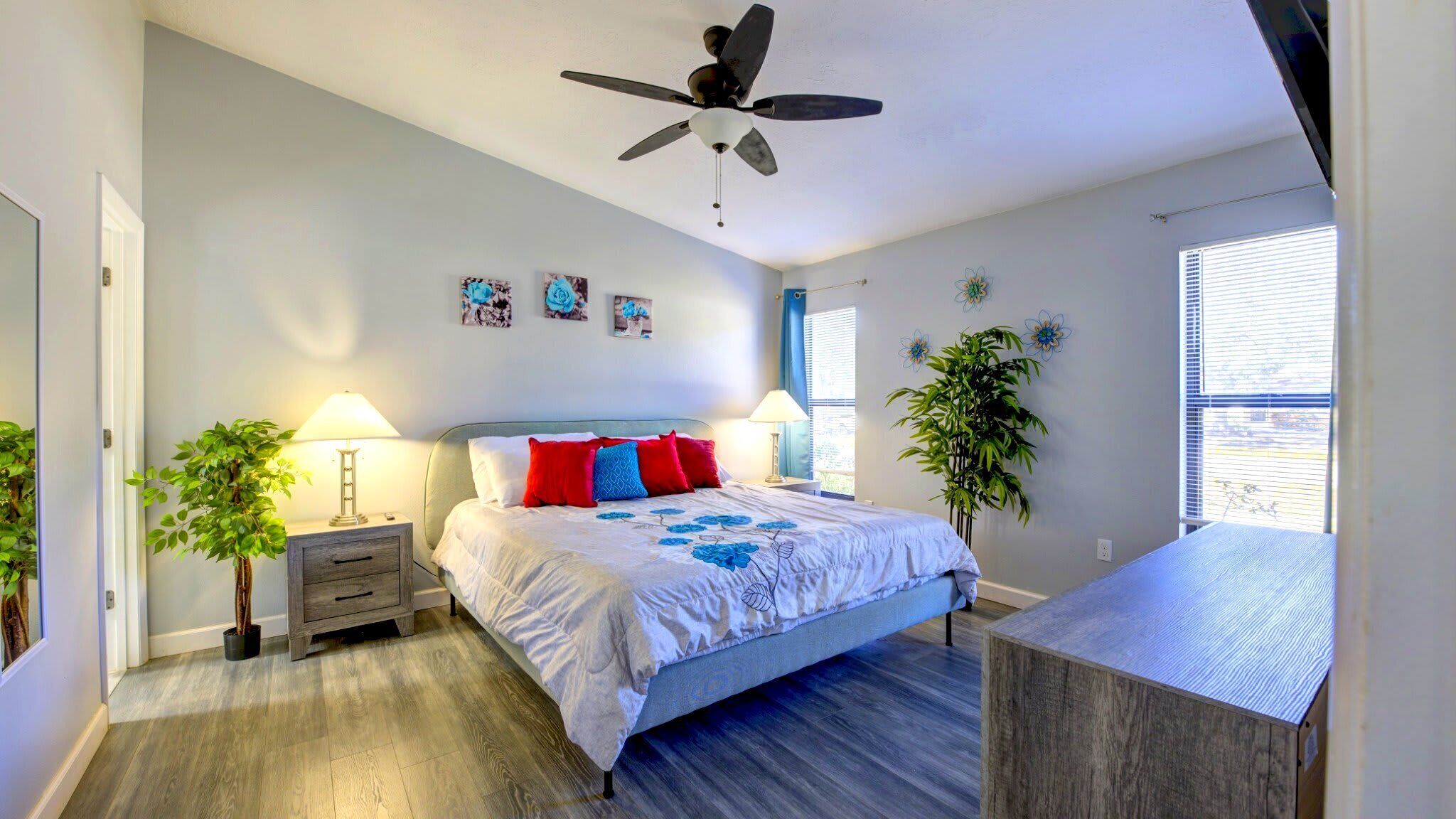 A bedroom with a bed, two bedside tables, a ceiling fan, and a window with blinds.