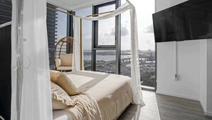 A bedroom with a large window, a bed, a chair, and a black TV. - Downtown Miami 2BR Skyline Bay View Balcony Corner Suite Luxepad (Miami)