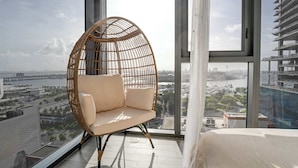 A high-rise room with a large window, a wicker chair, and a bed. - Downtown Miami 2BR Skyline Bay View Balcony Corner Suite Luxepad (Miami)