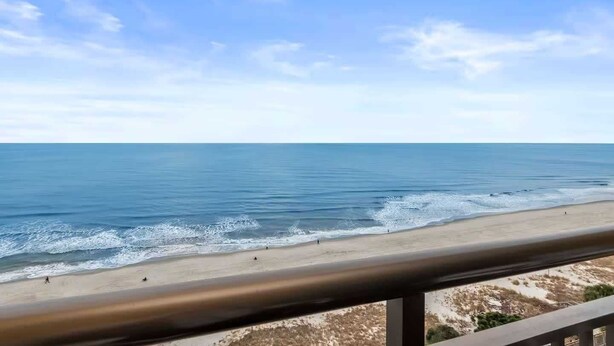 A beach view with a clear sky, a sandy shore, and a metal railing. - Caravelle 1445 (Myrtle Beach)