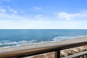 Une vue sur la plage, avec un ciel dégagé, une plage de sable et une rambarde en métal.