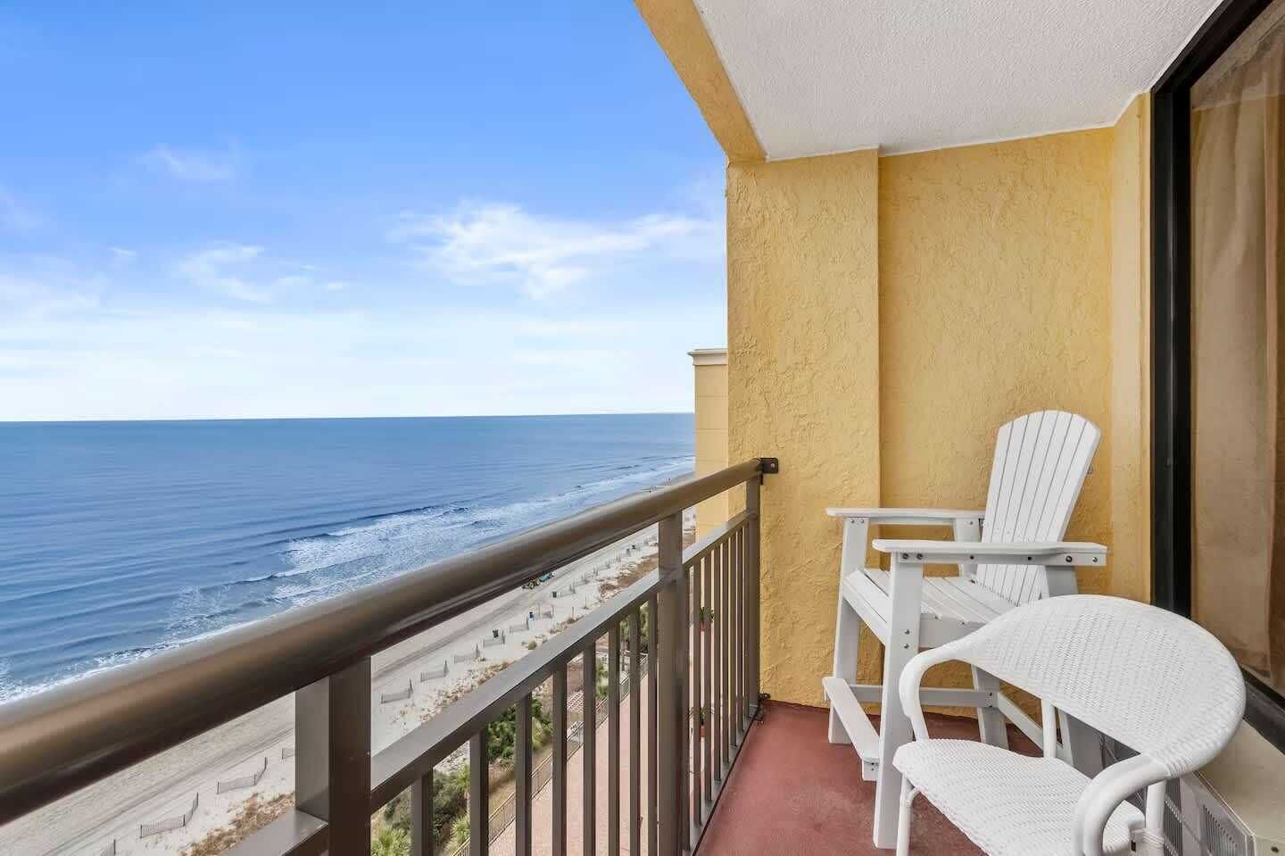 A balcony with a view of the ocean, white chairs, and a yellow wall.