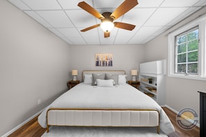 A bedroom with a bed, ceiling fan, artwork, bedside lamps, and a TV. - Lake Como Condo With Lake Views and Pool (Lake Geneva)