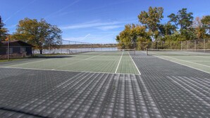 An outdoor tennis court with a net, surrounded by trees and a building. - Lake Como Condo With Lake Views and Pool (Lake Geneva)