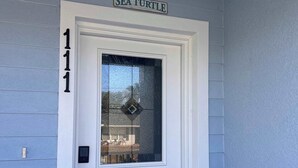 Eine weiße Tür mit einem Glasfenster, ein Schild mit der Aufschrift 'SEA TURTLE' darüber und die Zahl '1111' an der Wand.