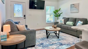 Ein modernes Wohnzimmer mit einem grauen Sofa, einem runden Couchtisch und einem an der Wand montierten Fernseher.