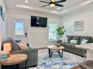 A modern living room with a grey sofa, a round coffee table, and a TV mounted on the wall. - Sea Turtle Hideaway Shell Yeah to Beach Vibes! (Punta Gorda)