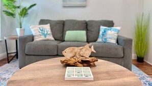 Ein Wohnzimmer mit grauem Sofa, dekorativen Kissen, einem Holztisch mit einer Fischskulptur und einer Schachtel Pralinen.