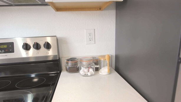 A kitchen with a stainless steel stove, three knobs, and a digital clock displaying 10:38. There are three glass jars with lids on the counter. - Relaxing Bargain Retreat With Hot Tub & BBQ (Cape Coral)