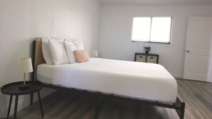 A bedroom with a bed, a bedside table with a lamp, a small cabinet, and a window with blinds. - Relaxing Bargain Retreat With Hot Tub & BBQ (Cape Coral)