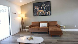 A living room with a brown sofa, a white coffee table, and a painting on the wall. - Relaxing Bargain Retreat With Hot Tub & BBQ (Cape Coral)