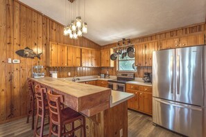 Eine Küche mit Holdekor, einem Edelstahlkühlschrank, einer Holztresenbar mit Barhocker und hängenden Töpfen.