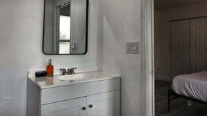 A bathroom with a white vanity, a mirror, a sink, and a toilet. There is a door leading to another room. - Cozy 2br Apartment in Cape Coral With Hot Tub U201 (Cape Coral)