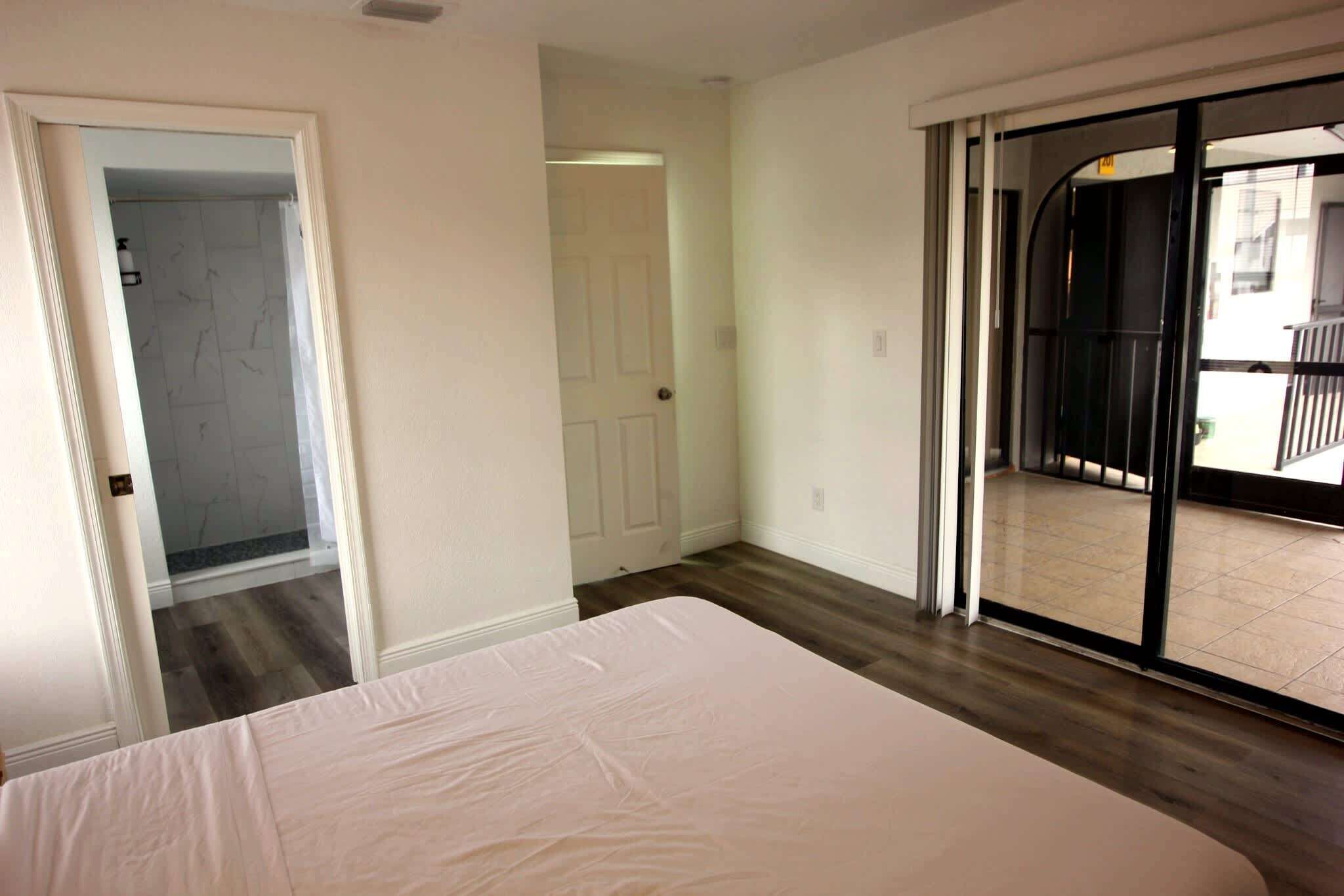 Ein Schlafzimmer mit einem großen Bett, einer Tür zu einem Badezimmer und einer Glastür zum Balkon.