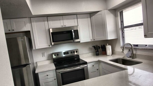 A modern kitchen with white cabinets, stainless steel appliances, a microwave, stove, and a sink. - Cozy 2br Apartment in Cape Coral With Hot Tub U201 (Cape Coral)
