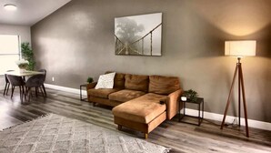 A modern living room with a sectional sofa, a dining table with chairs, a coffee table, a floor lamp, and a painting on the wall. - Cozy 2br Apartment in Cape Coral With Hot Tub U201 (Cape Coral)