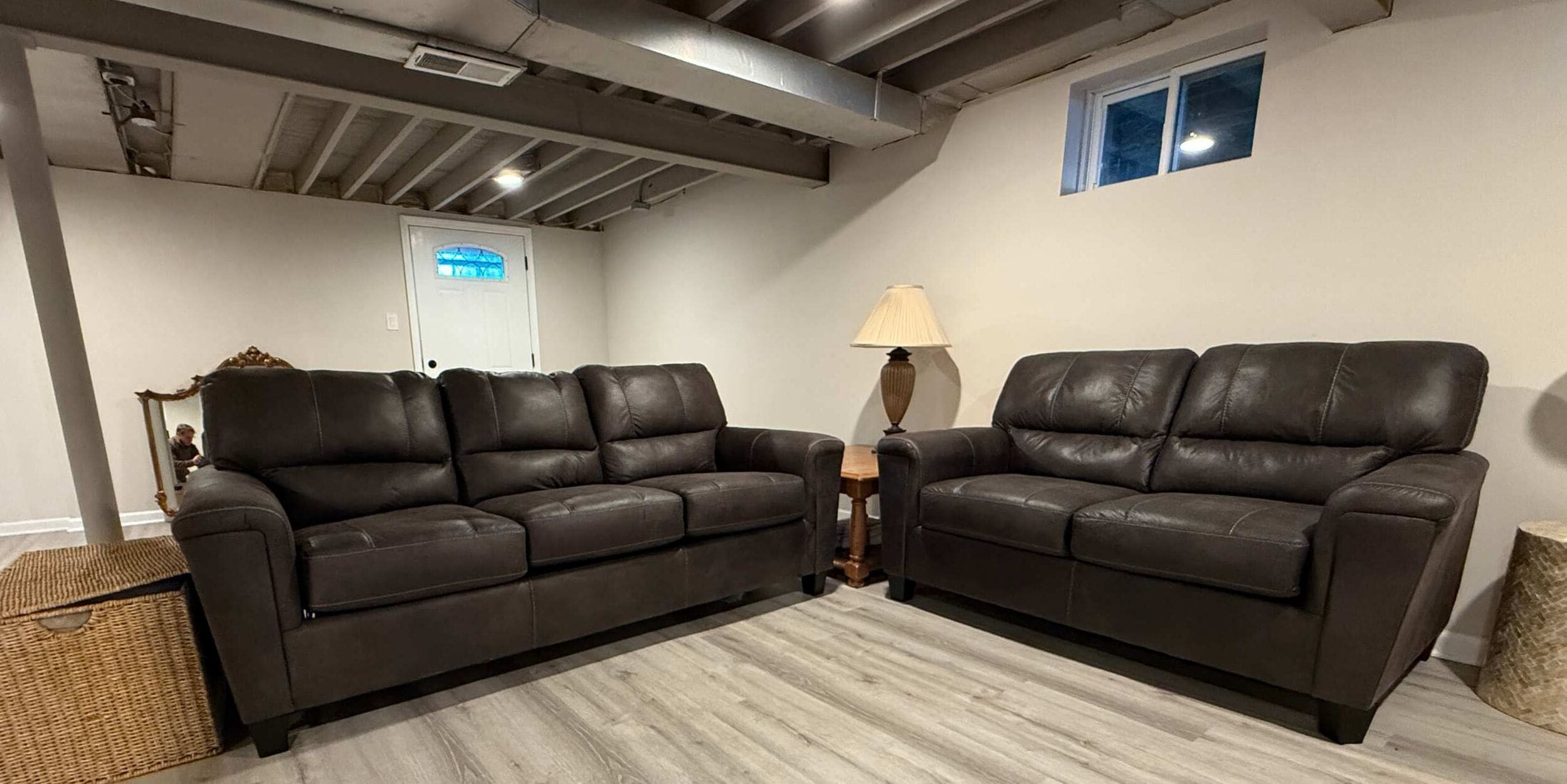 Ein Wohnzimmer mit zwei dunkelbraunen Ledersofas, einem kleinen Holztisch, einer Lampe und einem Fenster.