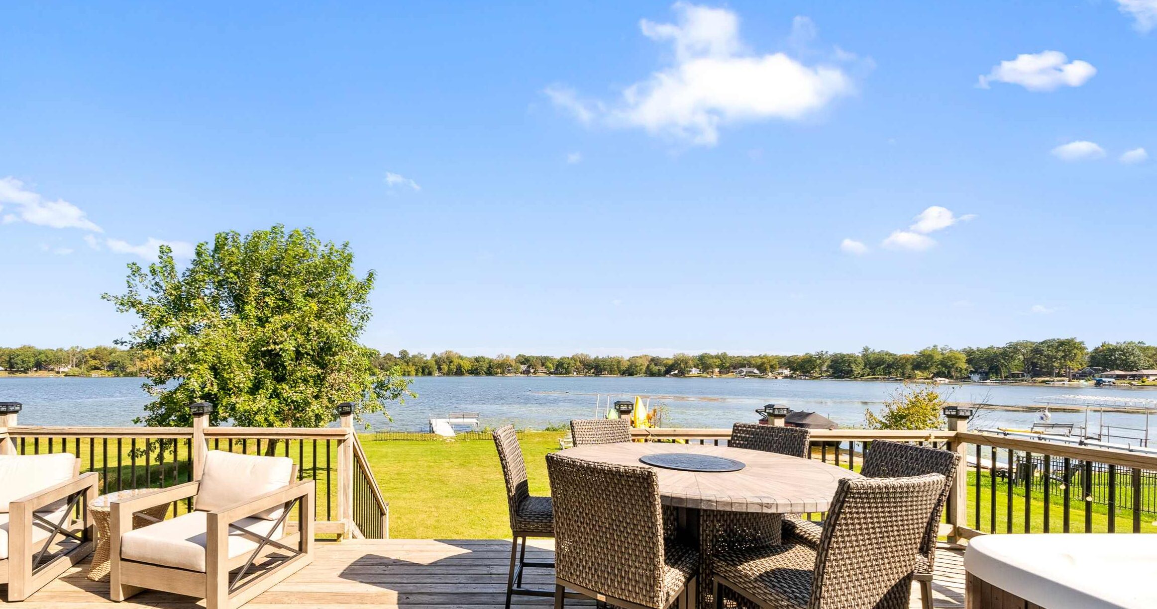 A deck with wicker furniture overlooking a lake.
