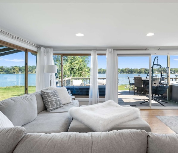 Una sala de estar moderna con un sofá grande, un plaid blanco y mullido, y vistas a un lago y una terraza.