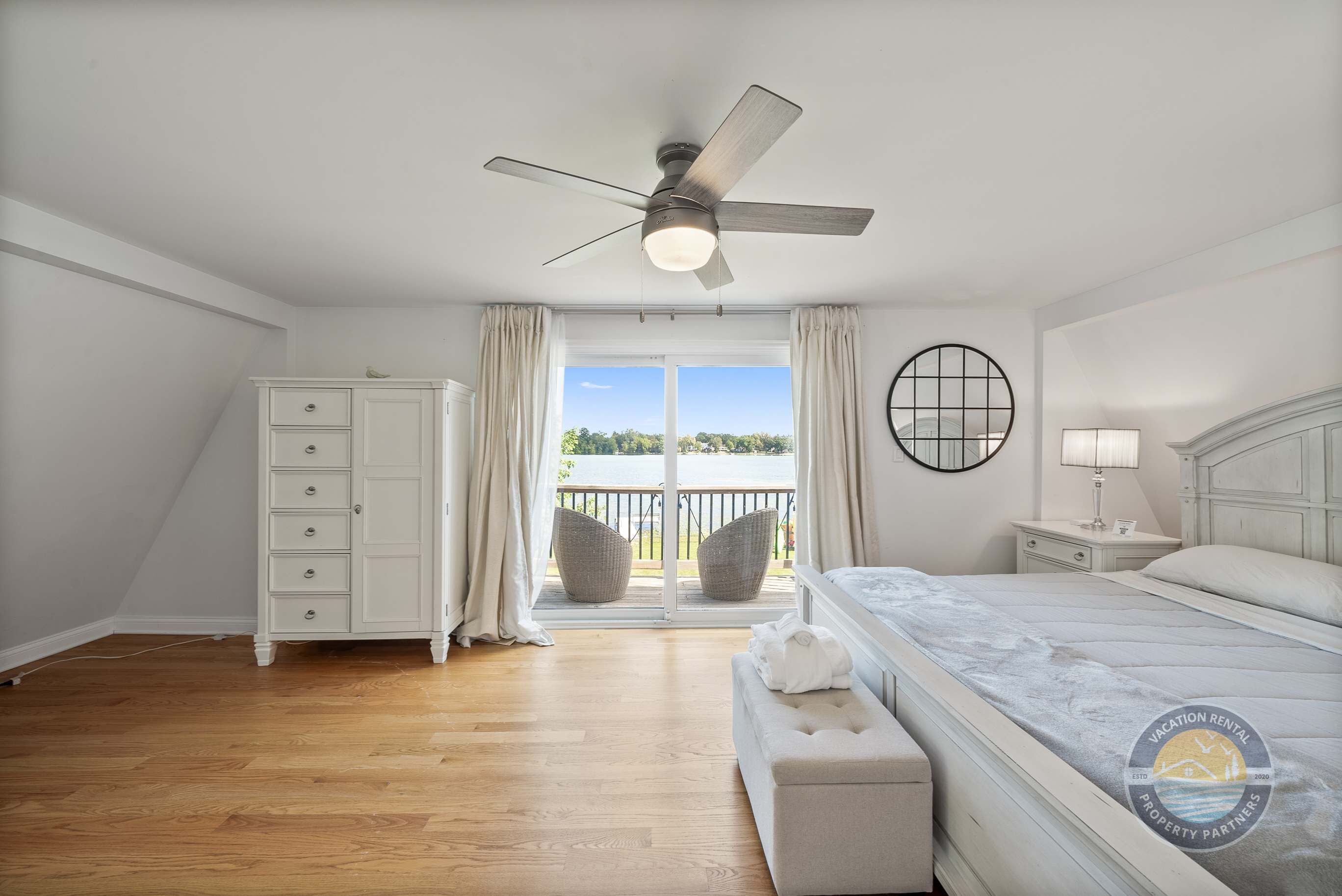 A bedroom with a bed, a nightstand, a dresser, a ceiling fan, and a view of the outdoors through a sliding glass door.