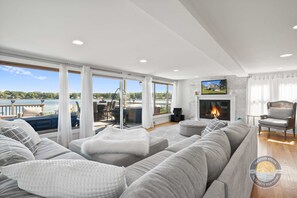 A spacious living room with a large gray sectional sofa, a fireplace, and a view of a lake.
