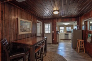 A wooden-paneled room with a dining table and chairs, a kitchen area with appliances, and a framed picture on the wall. - Pet-Friendly Gulf-Front 3BR with Screened Porch (Alligator Point)