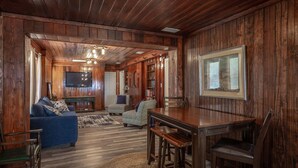 Interior em madeira com sofá, mesa de jantar e televisão.