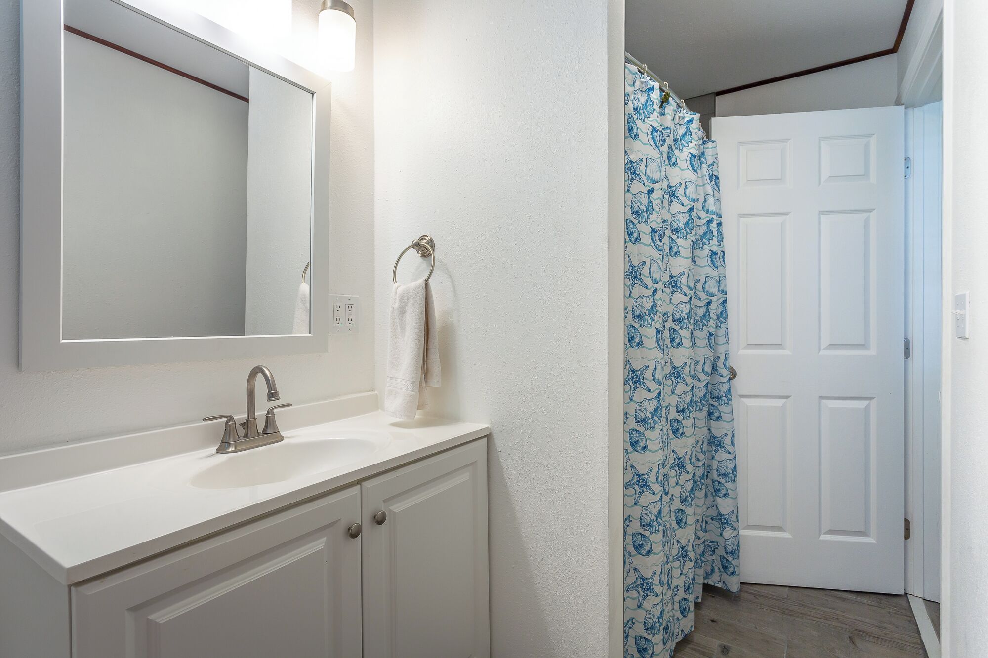 A bathroom with a white vanity, a mirror, and a shower curtain with a blue sea shell pattern.