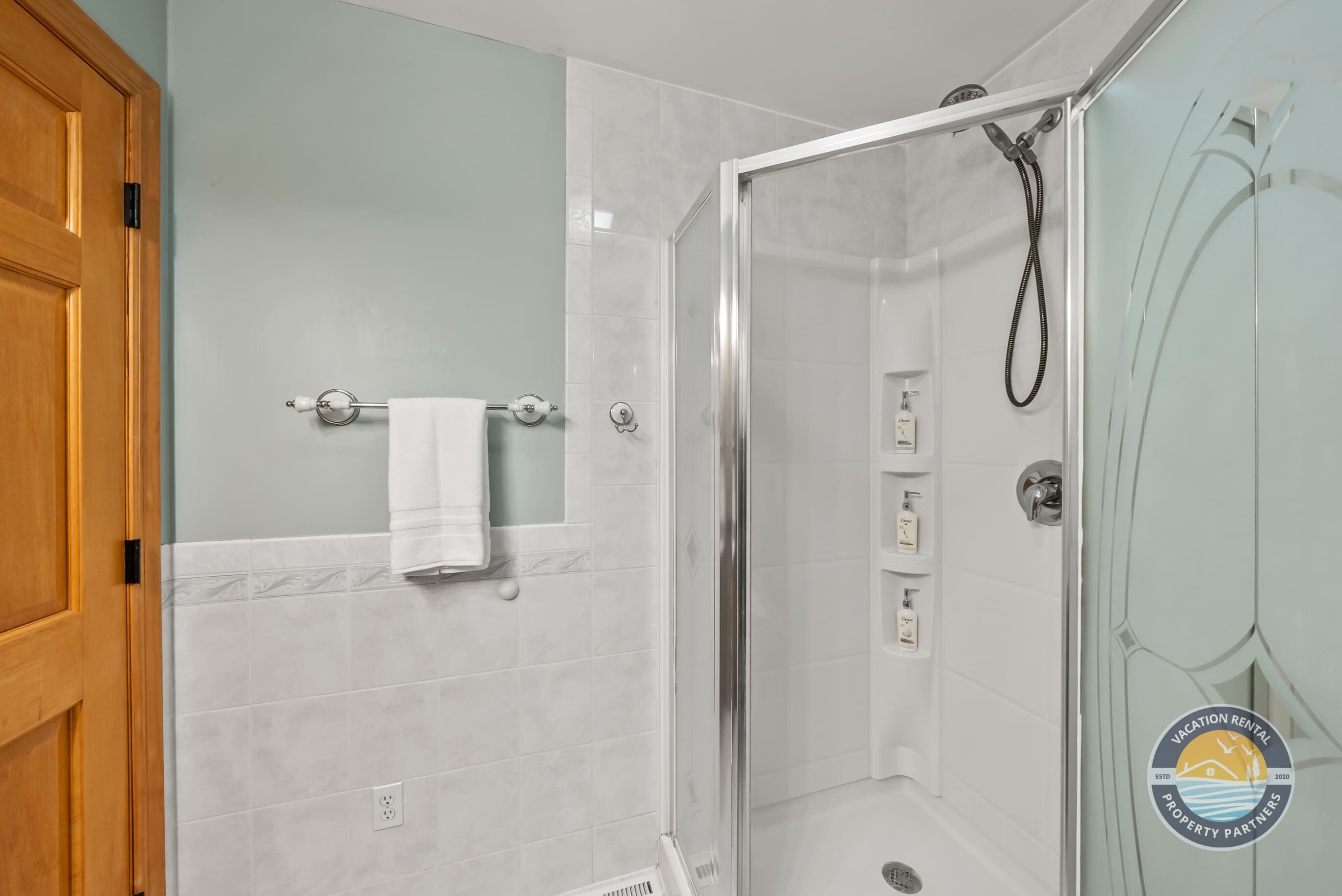 A bathroom with a glass-enclosed shower, a towel rack, and a wooden door.