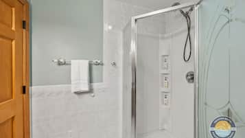 A bathroom with a glass-enclosed shower, a towel rack, and a wooden door.