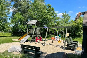 A playground with a slide, swings, and a wooden playhouse. - Exclusive Lake Como Escape With Bar and Pool Table (Lake Geneva)