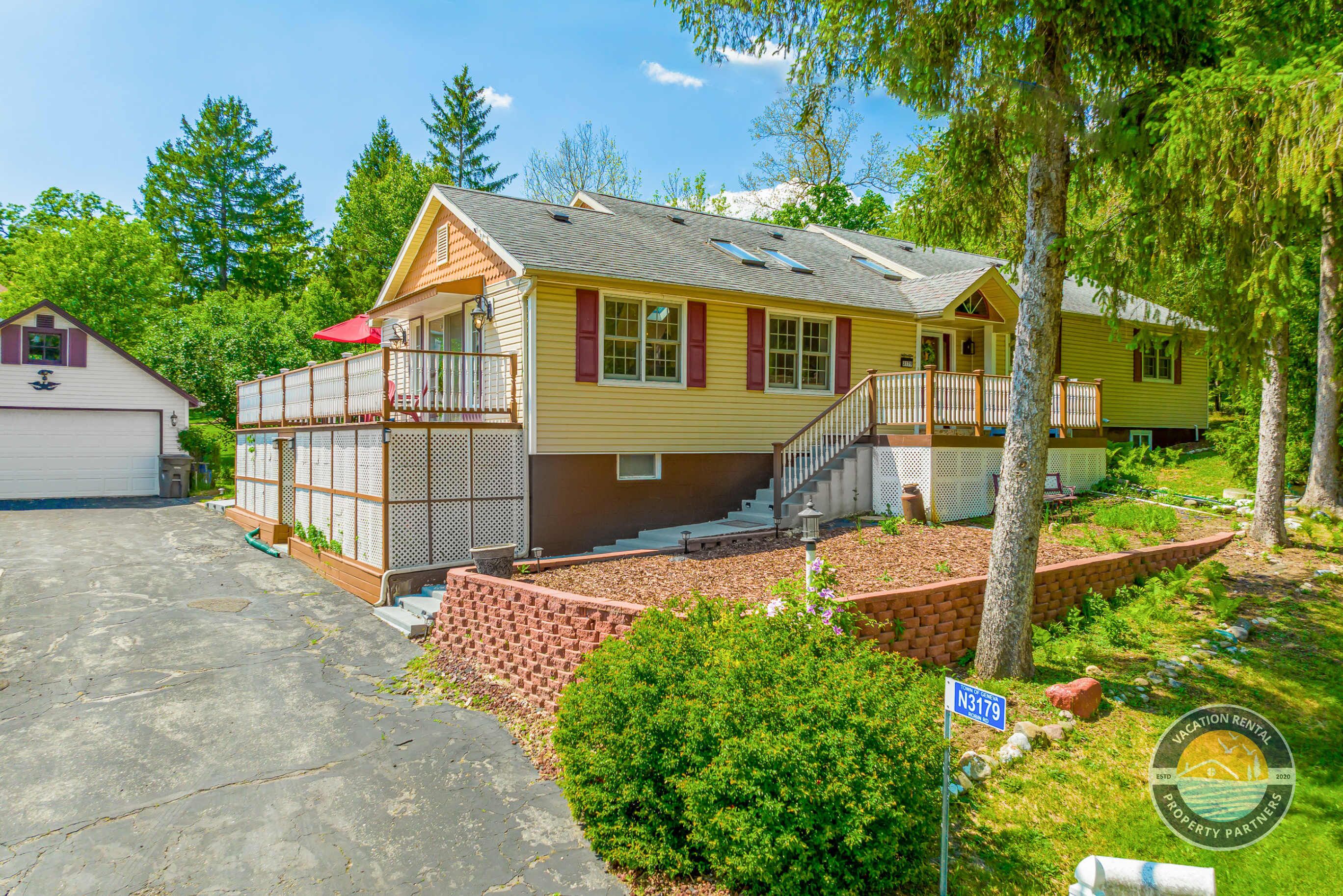 A two-story house with a front porch, a covered deck, and a brick pathway leading to the front door.