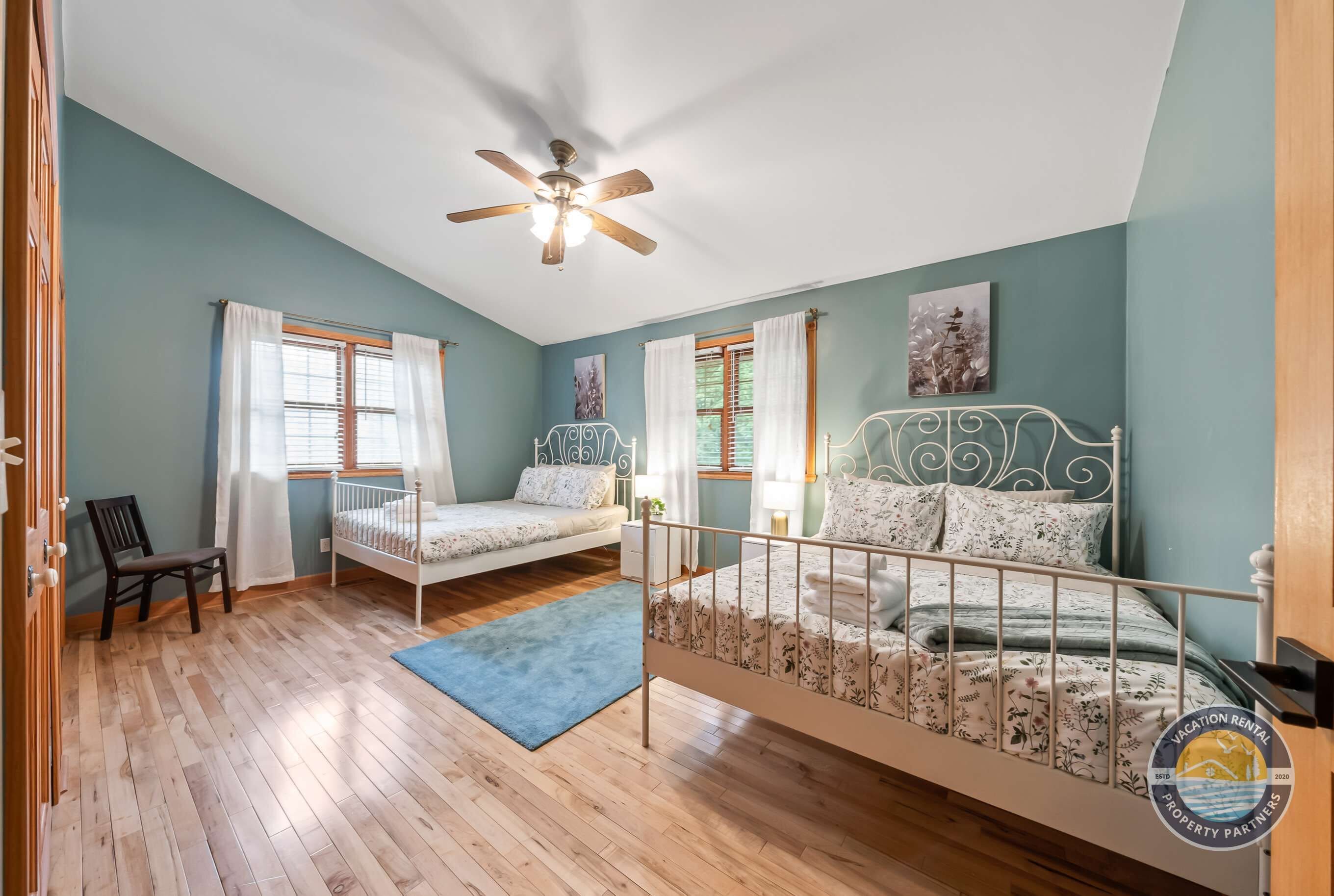 A room with a bed, a chair, a desk, a ceiling fan, and a window with curtains.