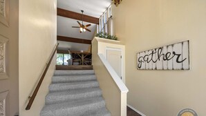 A staircase with a ceiling fan, a 'gather' sign on the wall, and a door leading to a dining area. - Modern Lake Geneva Condo With Views (Lake Geneva)