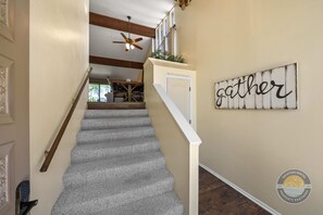 A staircase with a ceiling fan, a 'gather' sign on the wall, and a door leading to a dining area. - Modern Lake Geneva Condo With Views (Lake Geneva)