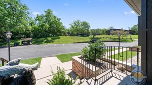 A building with a brick entrance, a parking lot, and a view of a green park with trees and a clear sky. - Modern Lake Geneva Condo With Views (Lake Geneva)