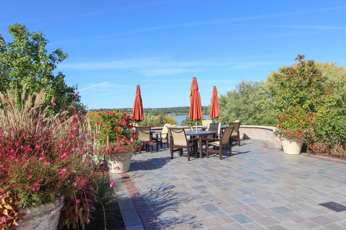 An outdoor patio with stone flooring, tables, chairs, and red umbrellas.