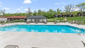 A swimming pool with lounge chairs and a small building, surrounded by a fence and greenery. - Modern Lake Geneva Condo With Views (Lake Geneva)