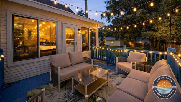An outdoor patio with string lights, a sofa, and a glass table. - Walk to Lake Relaxing Williams Bay Getaway (Williams Bay)