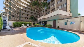 Um edifício de vários andares com piscina, espreguiçadeiras e portão fechado.