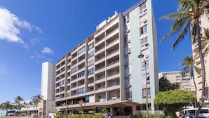Ein mehrstöckiges Hotel mit zentralem Eingang, Balkonen und einem Parkplatz.