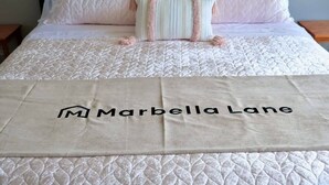 A bed with a quilted bedspread and a beige blanket with "Marbella Lane" embroidered on it. - Marbella Lane - Waikiki Studio Beach 15 Steps (Honolulu)