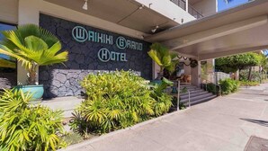 The exterior of the Aikiki Grand Hotel with a stone facade, palm trees, and a clear blue sky. - Marbella Lane - Waikiki Studio Beach 15 Steps (Honolulu)