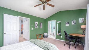 A bedroom with a bed, a desk with a chair, a ceiling fan, and a bathroom visible through an open door. - Modern 3-br Townhome w Private Backyard Near RTP (Morrisville)