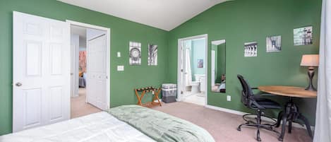 A bedroom with a bed, a desk with a chair, a ceiling fan, and a bathroom visible through an open door.